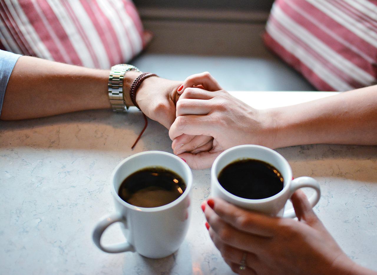 a man and a women siting on a table holding hands and having a cup of coffee